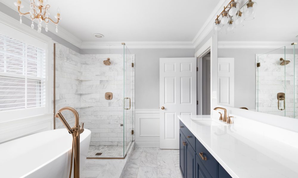 A beautiful bathroom with a blue vanity cabinet, standalone bathtub and shower, and gold faucets.